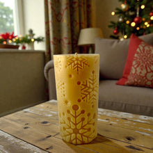 Load image into Gallery viewer, Decorative beeswax candle with snowflake patterns on a wooden table in a festive living room.