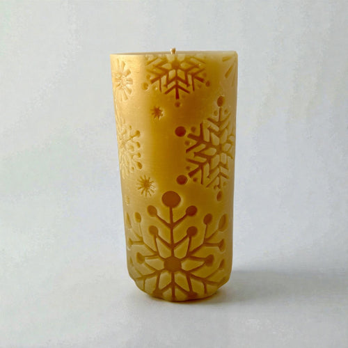 Beeswax candle with snowflake design on a light gray background